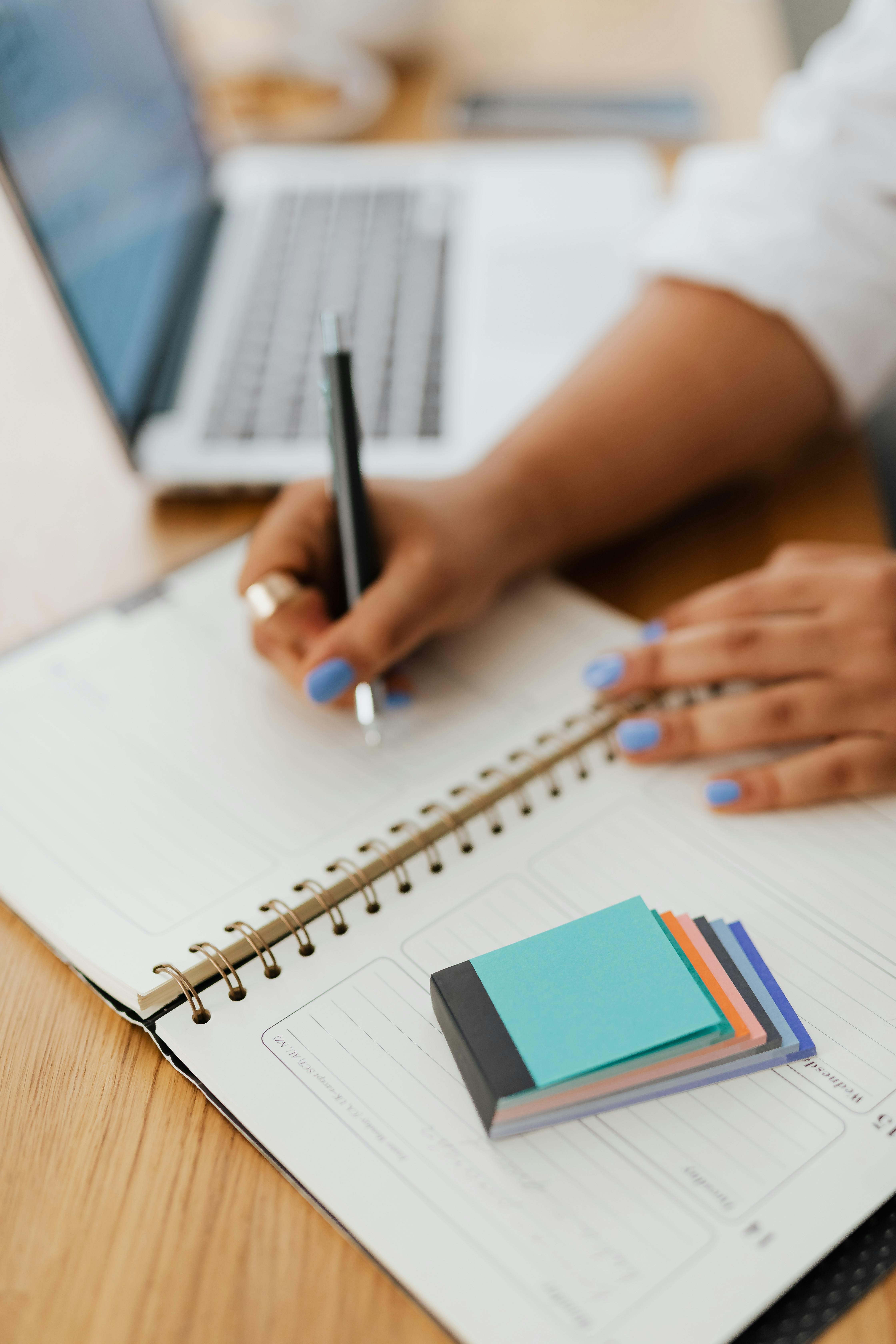 Hands writing on notepad a desk with laptop.